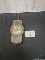 Front view of rusted metal hanging scale showing dial, hook and ring