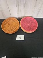 Two stacks of round wicker plate holders, one natural tan, one pink, showing weave detail