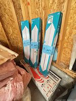 Three blue boxes of T8 tubes beside several sealed fixture cartons against wall