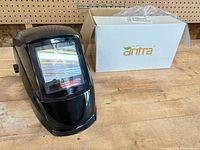 Front view of Antra welding helmet beside original box