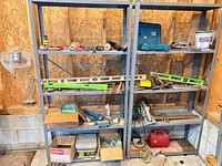 Overall view of two shelving units with assorted tools, levels, adhesive bucket, fuel can and hardware