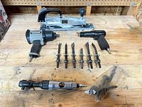 All four air tools with chisels and bag of extra bits laid out on workbench