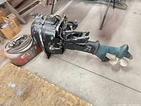 Outboard motor lying on floor with propeller, cowl, lower unit visible alongside gas tank