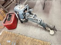 Overall view of outboard motor lying on floor next to red fuel tank