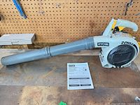 Full view of Ryobi gas leaf blower with manual on workbench