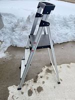 Full view of three-step aluminum ladder folded open on driveway