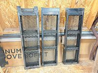 Three steel ramps standing upright, mesh tread visible