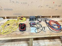 Overall lot: two battery chargers, booster cables, three extension cords on workbench