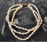 Bracelet laid flat showing three strands of rice pearls and the gold clasp