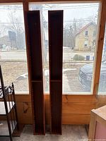 Front view of two tall narrow shelving units showing wood finish and height