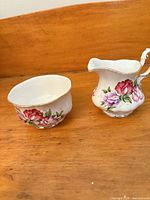 Cream pitcher and sugar bowl side by side showing floral design and shapes