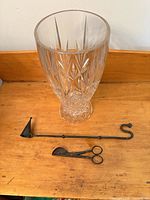 Crystal vase and two metal candle tools on wooden surface
