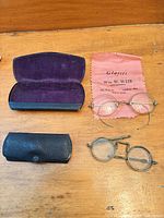 All lot items laid out: two eyeglasses, two cases, pink cleaning cloth