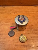 Tin with crest, medal badge, Canadian locket