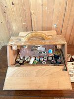 open wooden sewing box showing tray and multiple thread spools