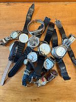 Pile of assorted wristwatches on wood surface showing variety of cases and straps