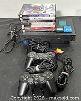 Full lot showing console, two controllers, stack of seven game cases, two blue memory cards and cables