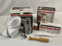 Three KitchenAid attachment boxes and parts displayed: slicer/shredder housing with drums, grinder parts, stuffer components
