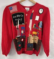 Full front view of red cardigan displaying embroidered classroom motifs