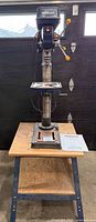 Full view of drill press mounted on workbench with manual on shelf