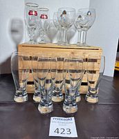 All 13 beer glasses arranged: 2 Stella Artois chalices, 4 Leffe goblets on crate, 7 pilsner glasses in front