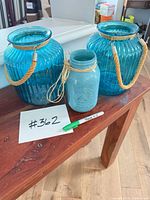 Front view of two ribbed blue glass vases with rope handles and painted mason jar