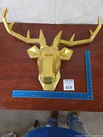 Front view of gold deer head sculpture with ruler for scale