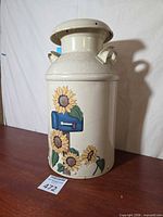 Front view of cream metal milk can with hand-painted sunflowers and blue mailbox, lid on