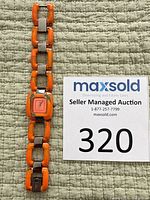 Front view of watch showing orange resin link bracelet and dial