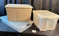 Three storage bins grouped: beige tote on clear under-bed bin, clear tote with blue rollers