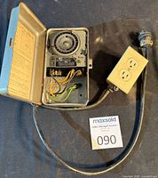 Overall view of open metal timer enclosure with attached cords and duplex outlet box