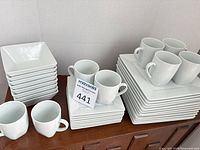 Full lot showing stacks of square dinner plates, bowls, mugs and dessert plates