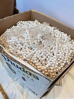 Open box showing large quantity of white round plastic beads and some clear acrylic beads