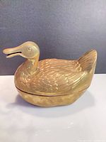 Side view of brass duck trinket box showing overall form and lid