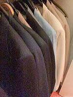 Row of assorted dark and light coloured blazers hanging in closet