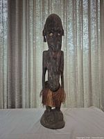 Full front view of standing wood figurine with raffia skirt
