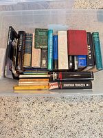 Plastic tote containing upright and stacked books showing spines