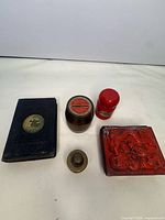 Group view of all five items: lacquer box, barrel bank, red cylinder, brass insert, black case