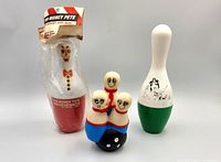 Three vintage bowling pin items: packaged Pin Money Pete bank, white/green kitty bank, Hartz dog squeak toy