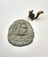 Brass figurine and stone welcome sign together for size comparison