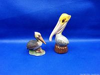 Front view of both pelican figurines against blue background