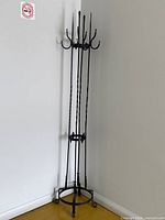 Full view of black wrought iron coat rack in corner showing overall structure and hooks