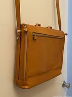 Side view of tan leather laptop bag showing zipper pocket and shoulder strap