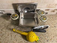 All items arranged: stainless pan and lid, three glass jars, whisk, citrus squeezer, peeler
