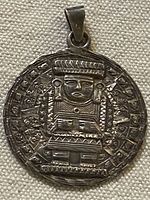 Front of round sterling silver pendant showing Aztec figure relief and bail