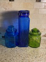 Front view of all three glass canisters showing color, shape, lids