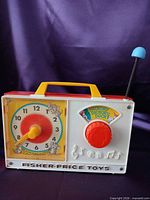 Front view showing clock dial, red knob, blue rod, Fisher-Price Toys branding