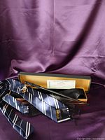 Wand in open box, tie, ticket and sleeve displayed on purple backdrop