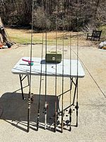 Eight fishing rods standing against table with closed tackle box visible