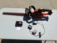 Cordless hedge trimmer, battery pack, charger and power cord laid out on table